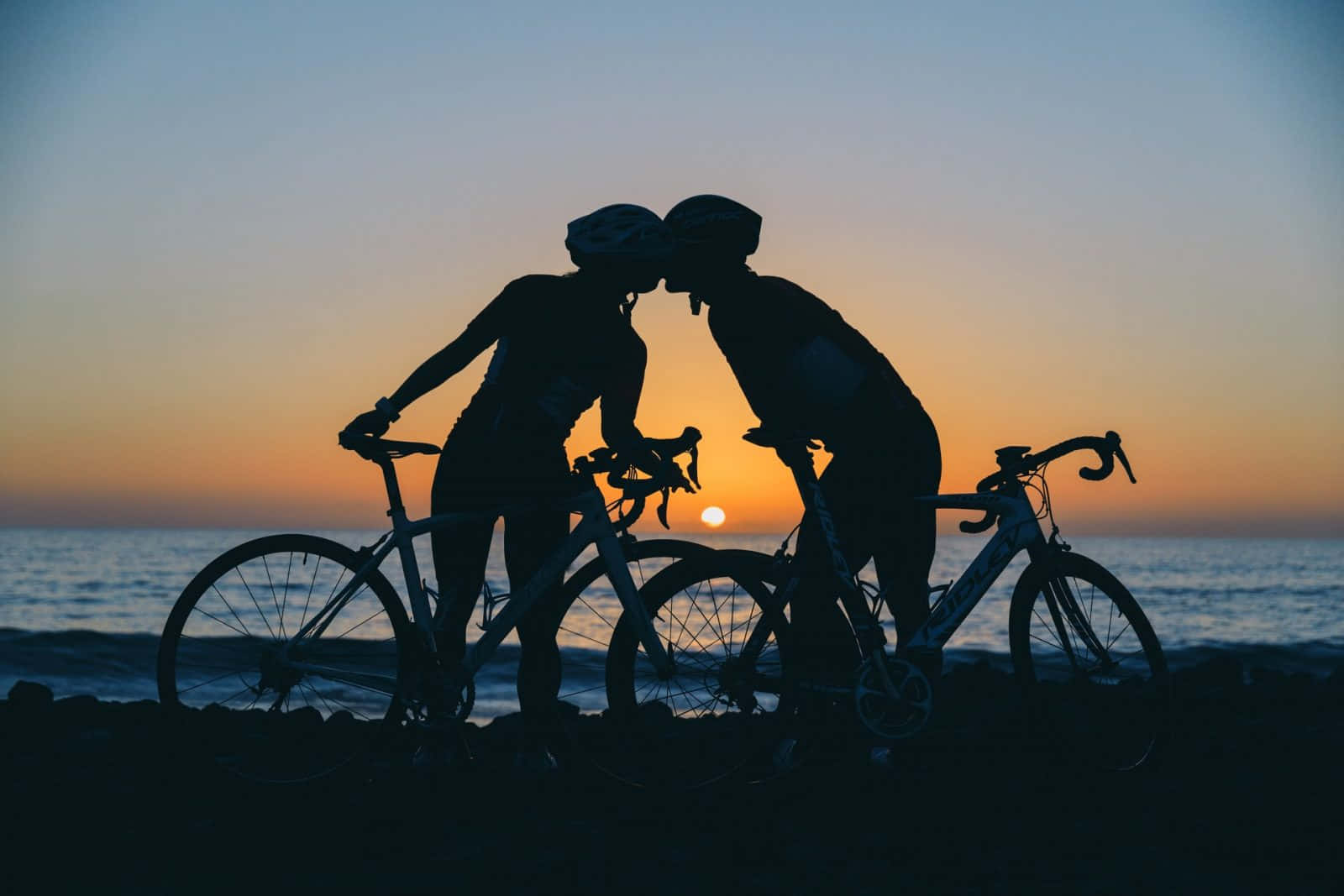 Two People Kissing On Their Bicycles At Sunset