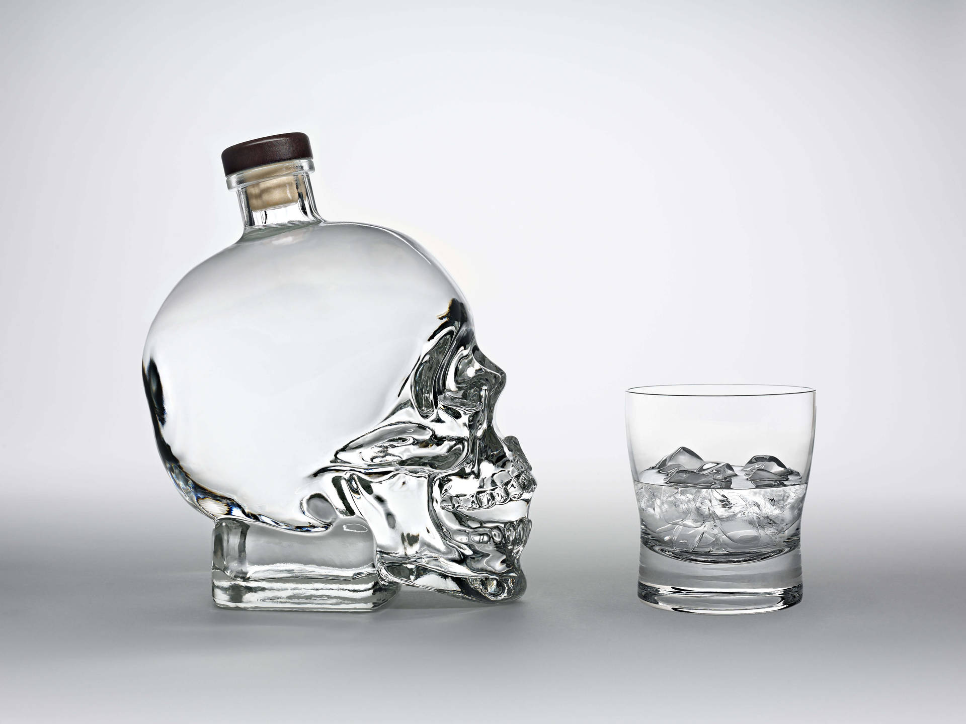 Crystal Head Vodka Bottle Facing A Glass Wallpaper