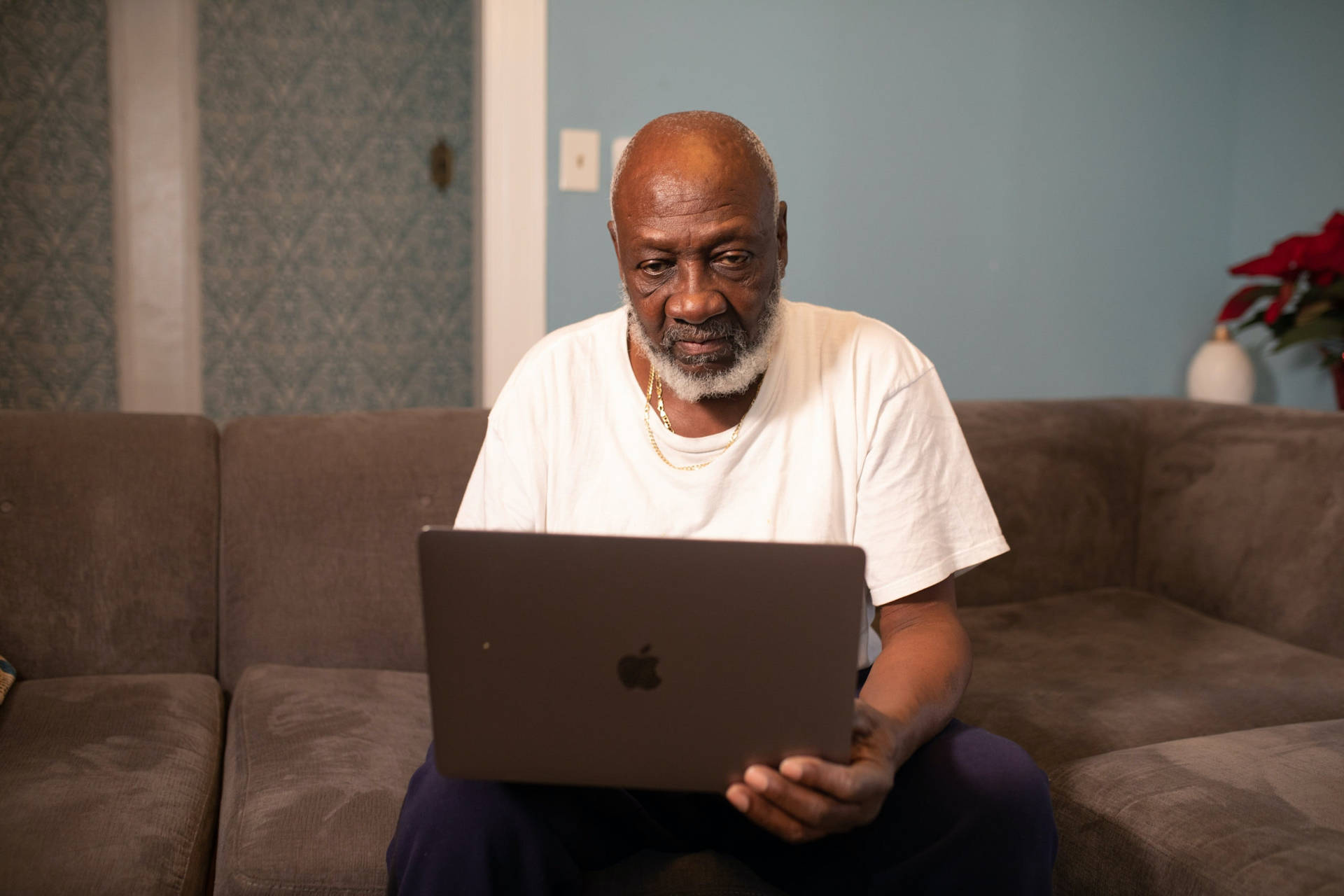 Old Black Man Using Laptop On Couch Wallpaper