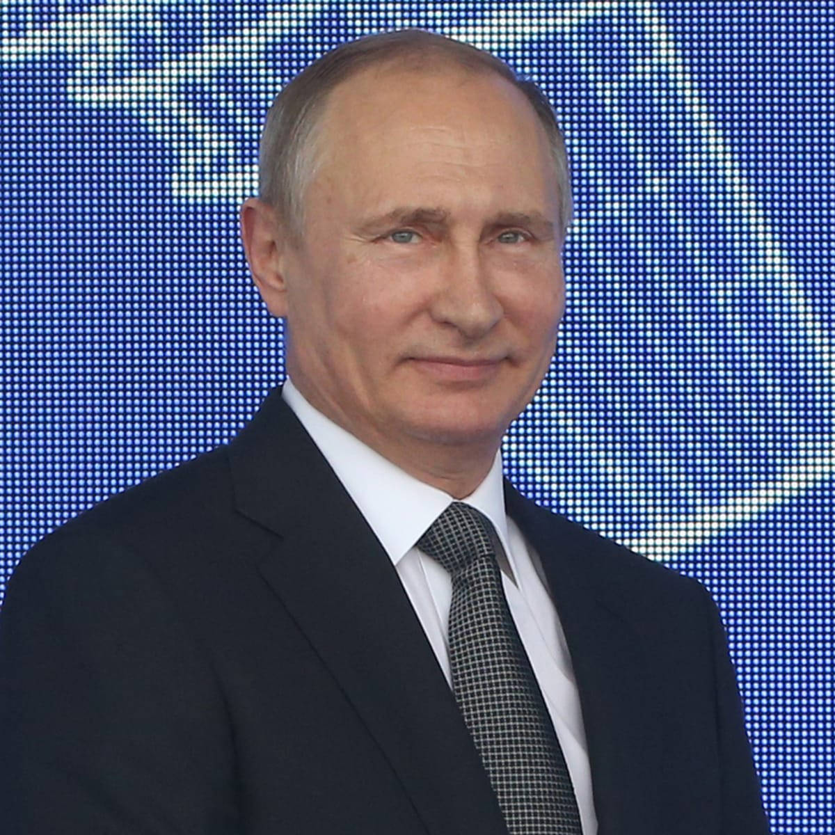 Russian President Vladimir Putin Smiling Against A Blue Background Wallpaper